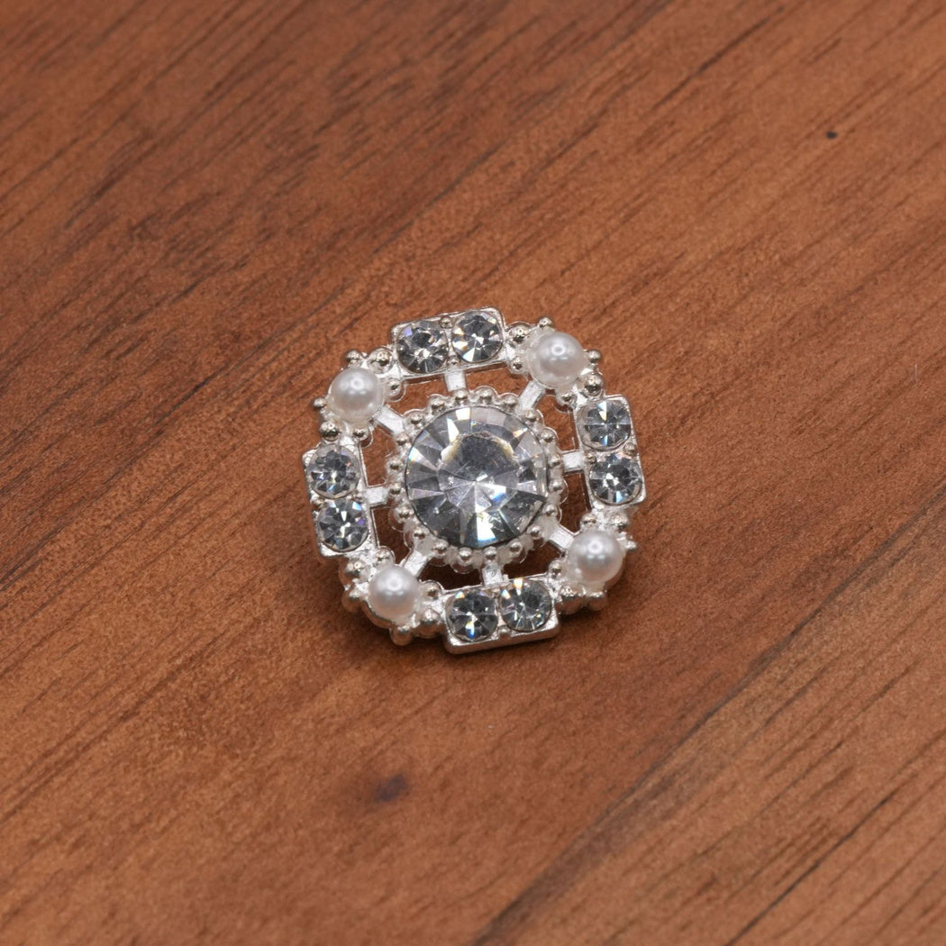 Open square silver-tone button with a clear faceted center, four white corner accents and paired clear side accents.
