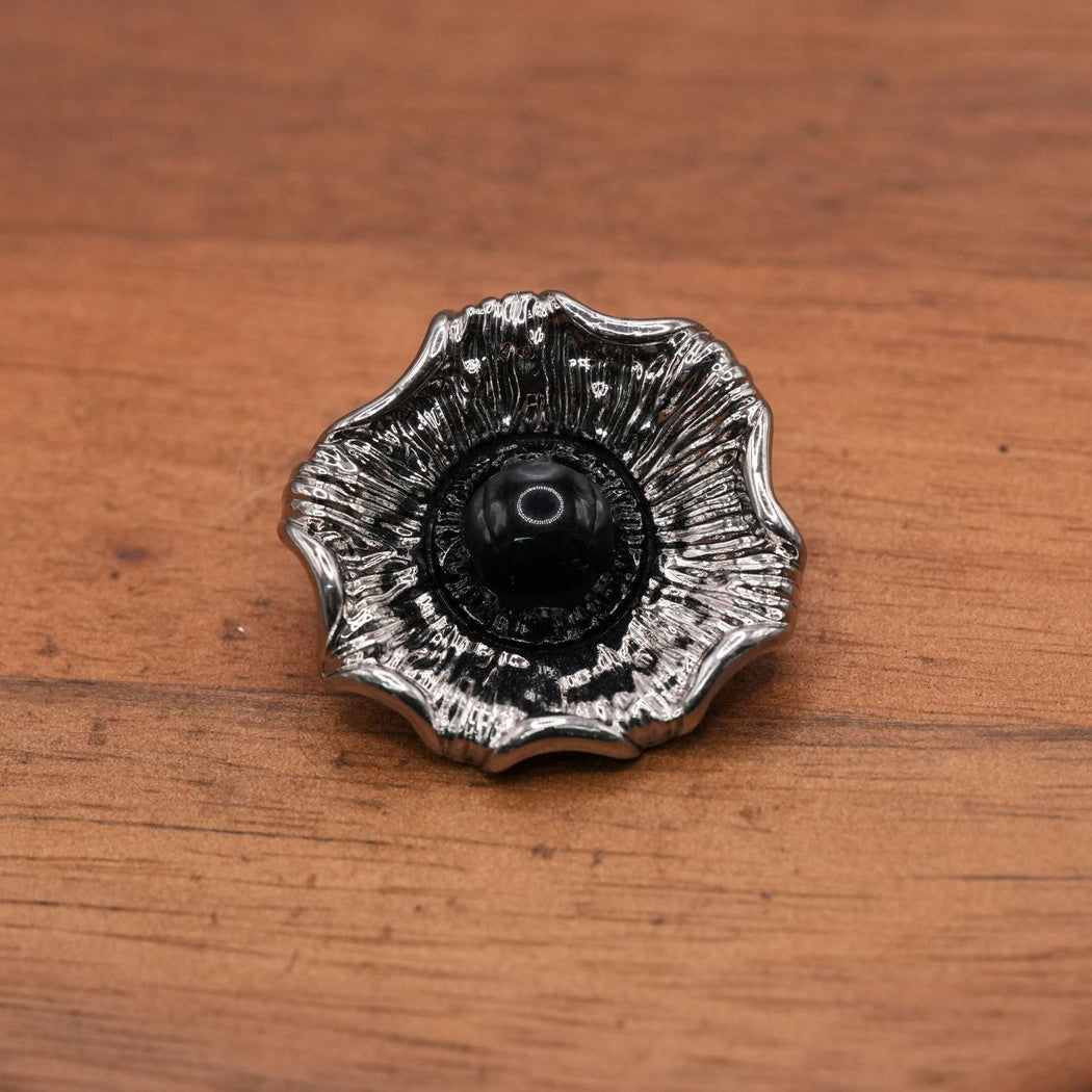 Silver-tone fluted flower button with a black domed center, single front view