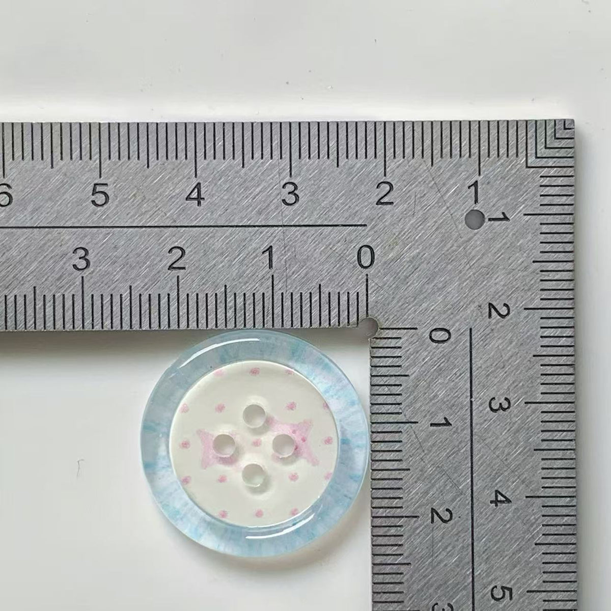 Aqua rim pink bow four hole button beside ruler