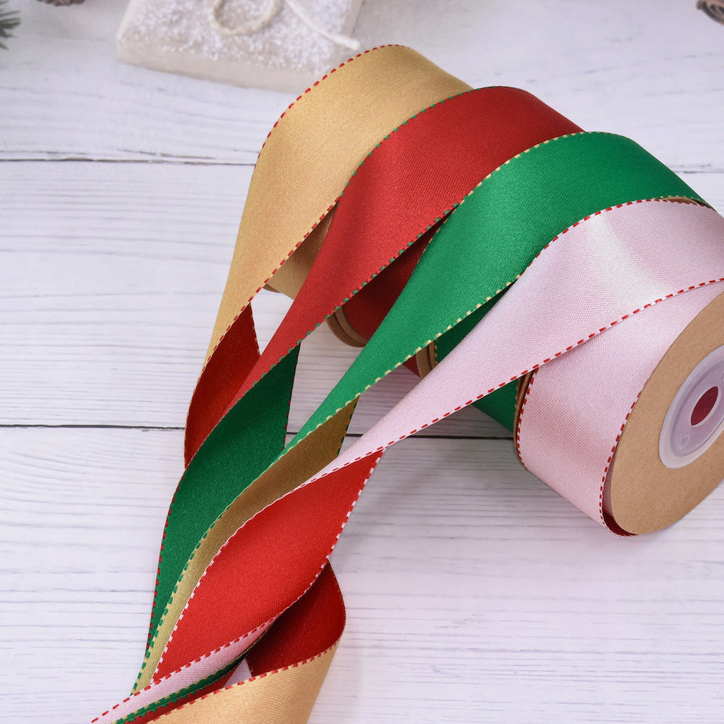 Gold red green and white stitched satin ribbon rolls on pale wood