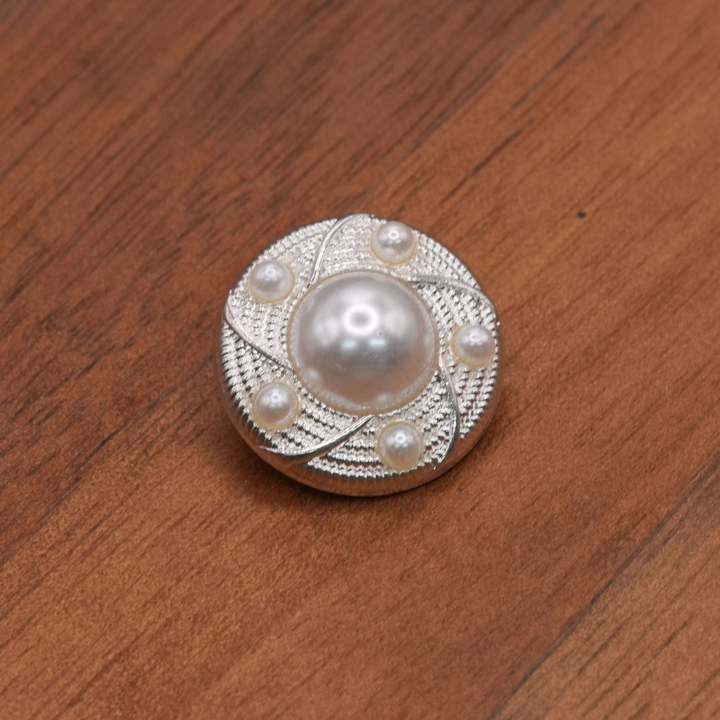 Round silver-tone button with a white domed center, five smaller white accents and curved textured sections.