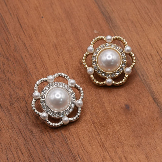 Silver-tone and gold-tone flower buttons with white domed centers and clear accents on a brown surface.