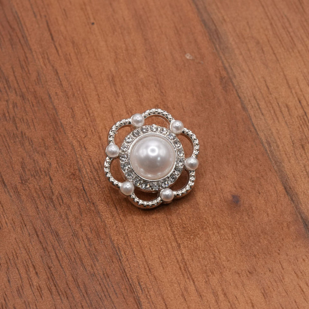 Silver-tone flower button with a white domed center, clear accents and six open petal loops.