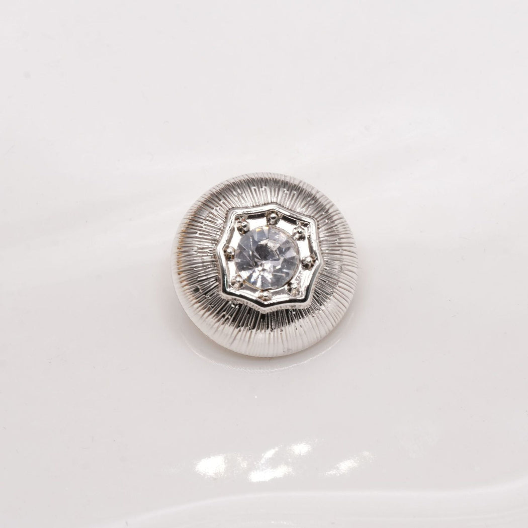 Silver-tone round button with radial grooves and a clear faceted center