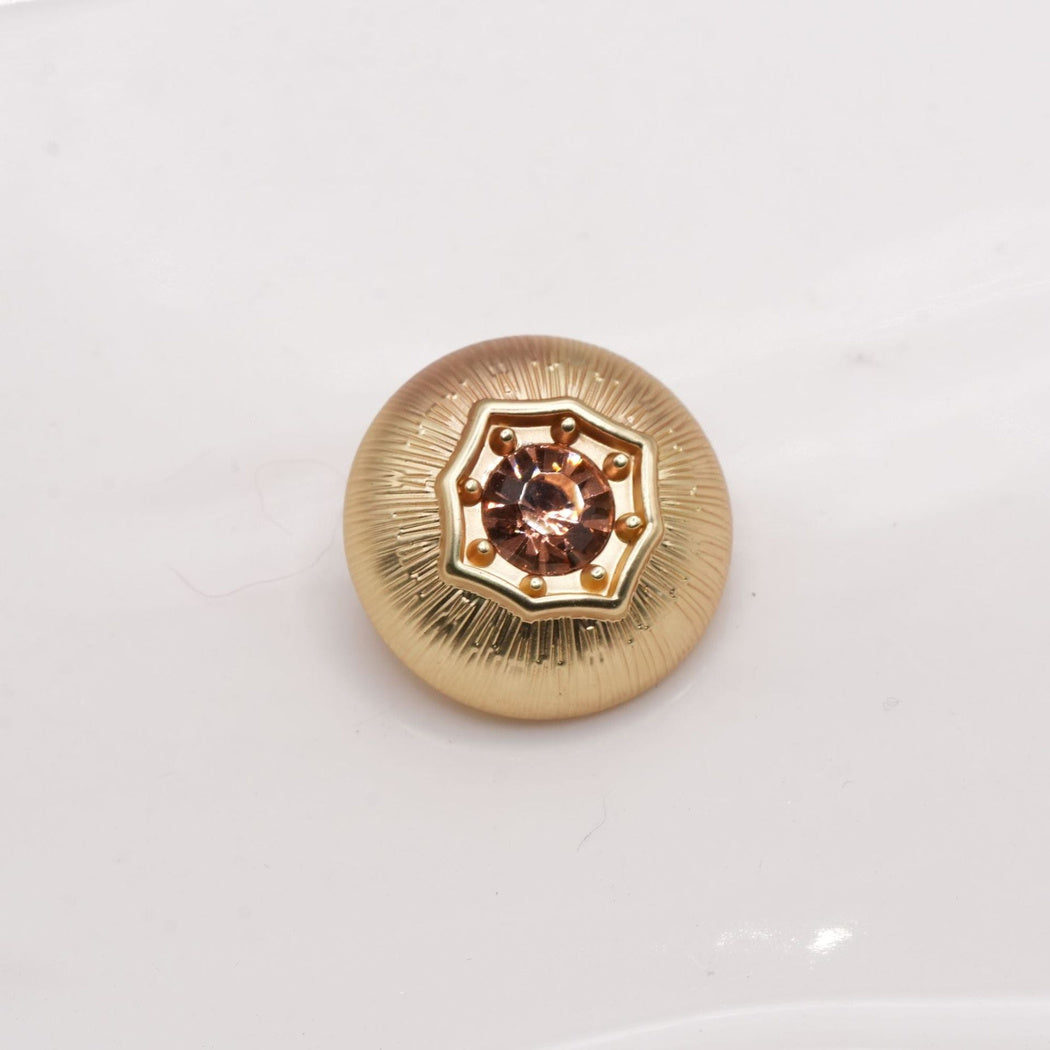 Soft gold-tone round button with radial grooves and a rose-colored center
