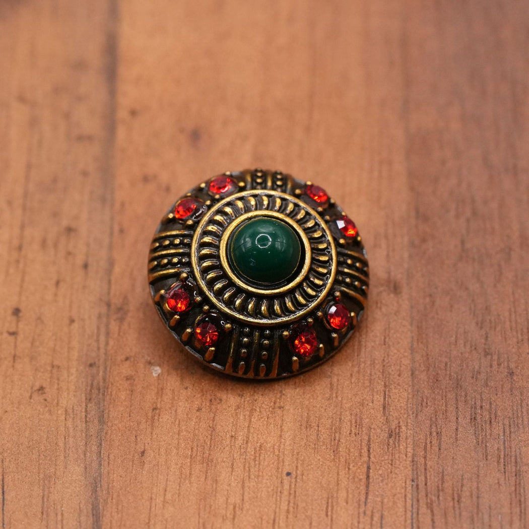 Round dark-green-center button with eight red accents and concentric raised rings