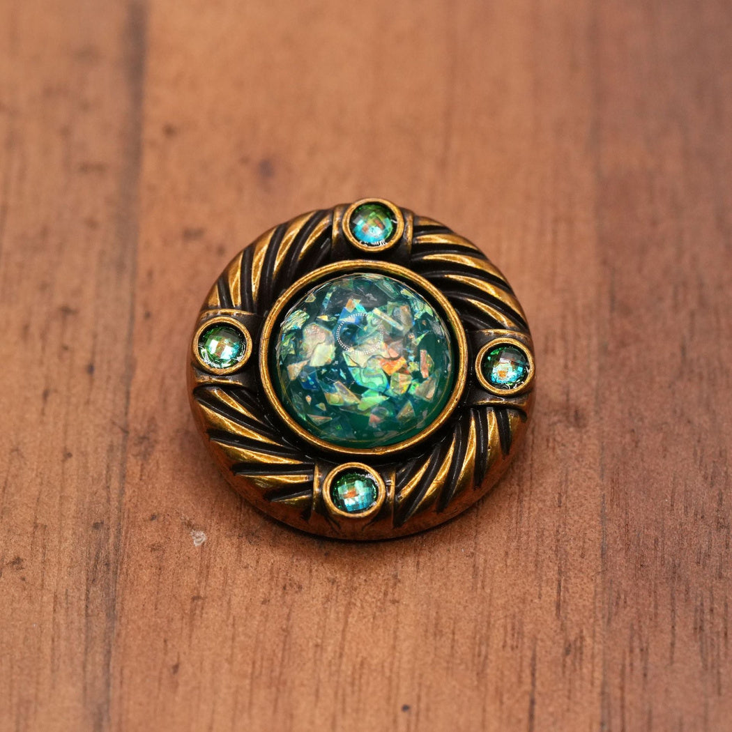 Round button with a mottled green center, four green accents and curved ridges