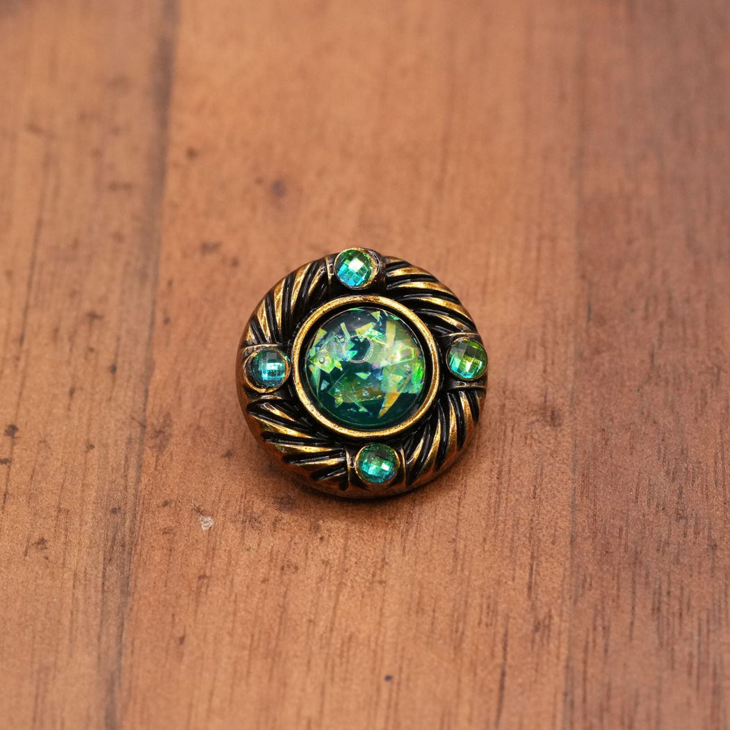 Small round button with an angular green iridescent center and four green accents