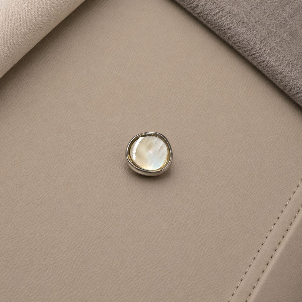 Silver-tone rimmed button with a pale cream center and fine diagonal bands