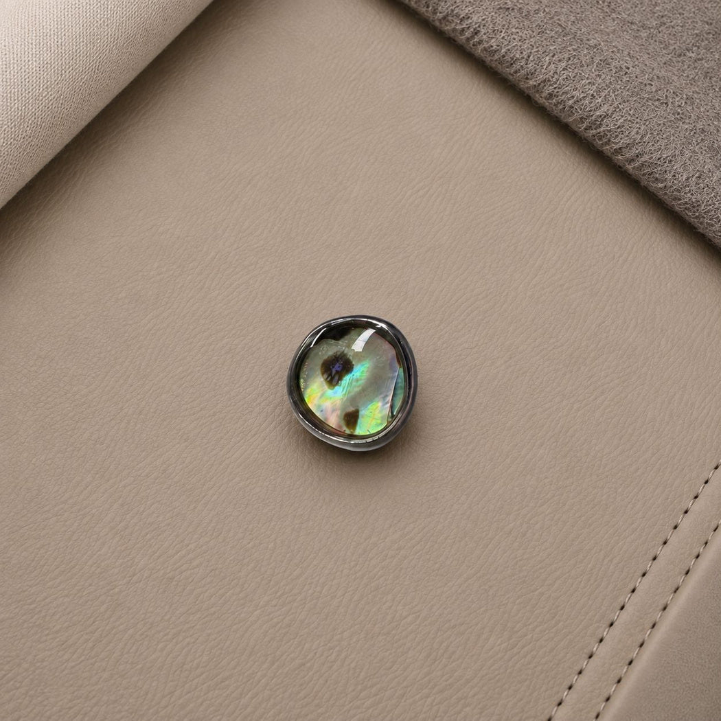 Silver-tone rimmed button with a dark mottled center and green and yellow highlights
