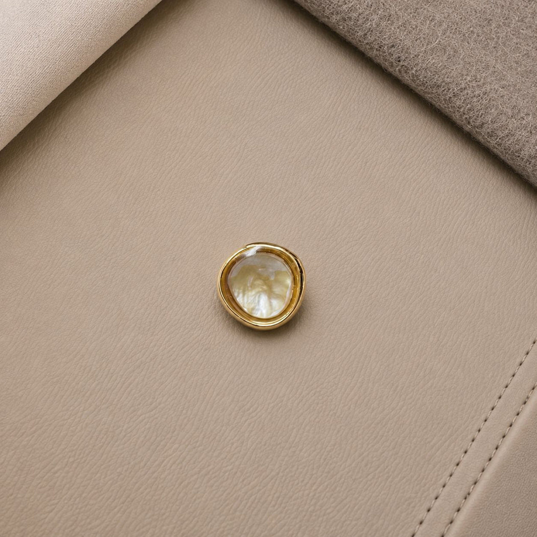 Gold-tone rimmed button with a cream center and flowing pale swirls
