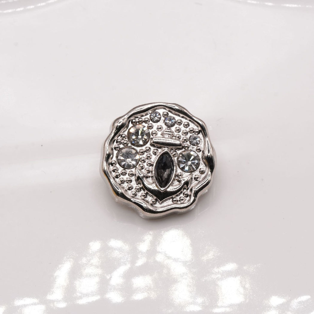 Silver-tone scalloped button face with a raised anchor and round accents.