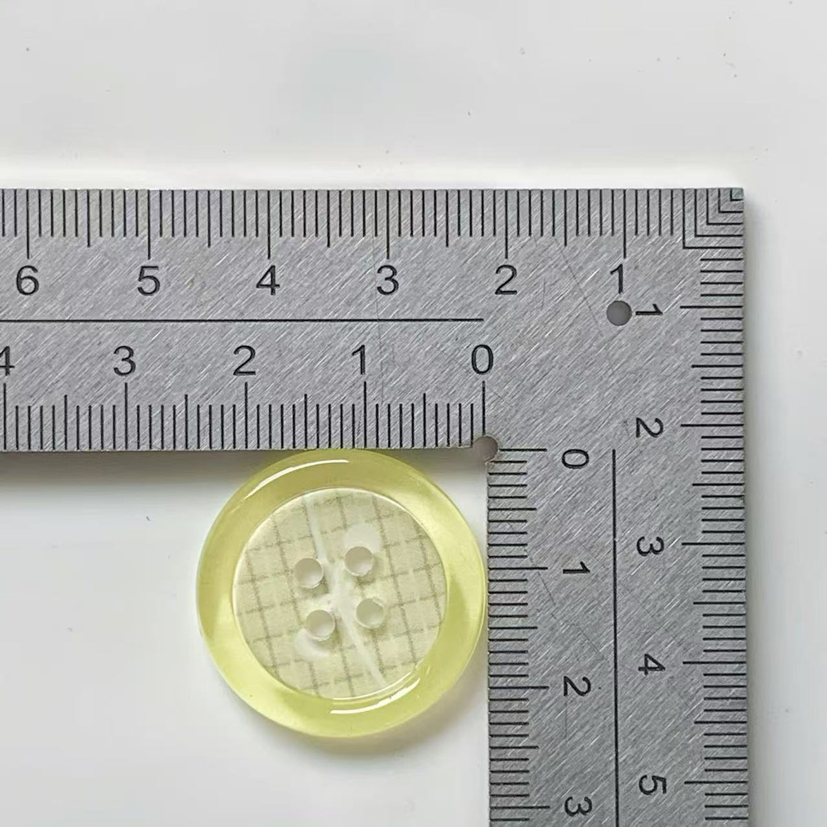 Yellow rim plaid four hole button beside ruler