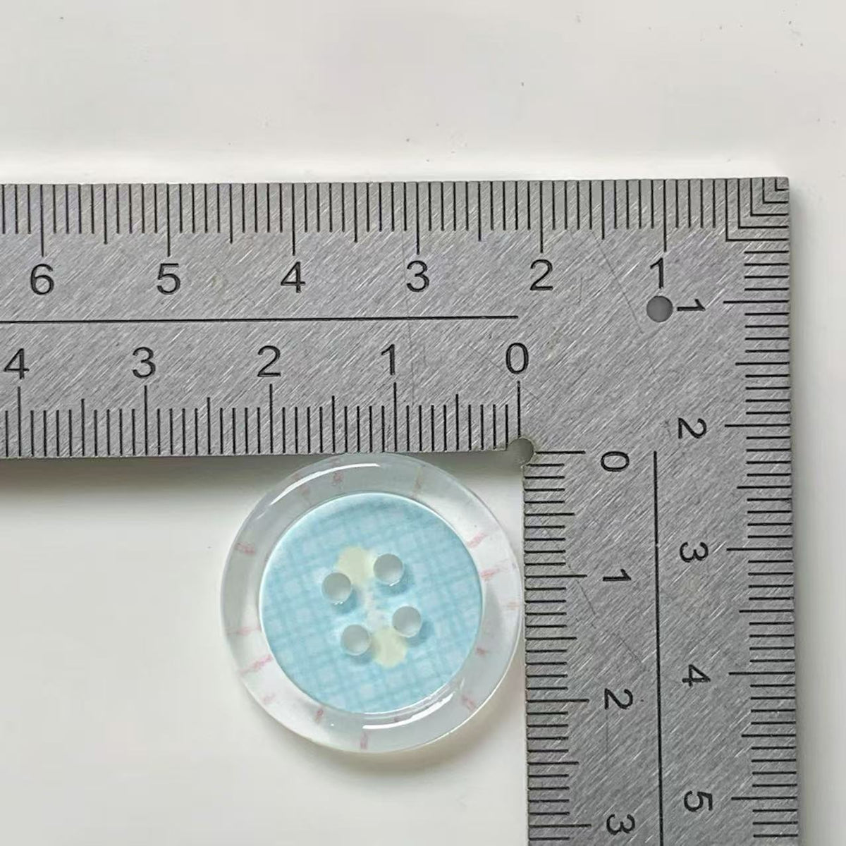 Aqua rim gingham four hole button beside ruler