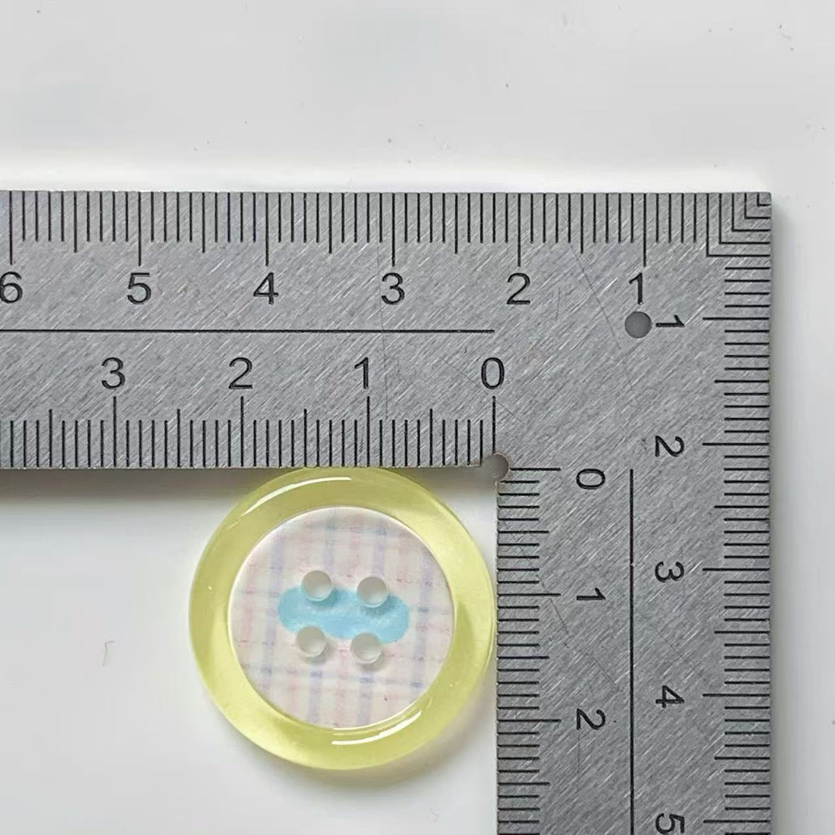 Yellow rim bow plaid four hole button beside ruler