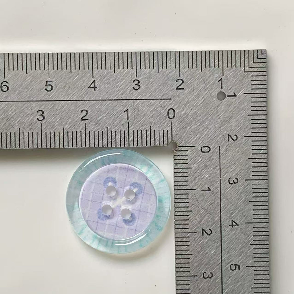 Aqua rim lilac loop four hole button beside ruler