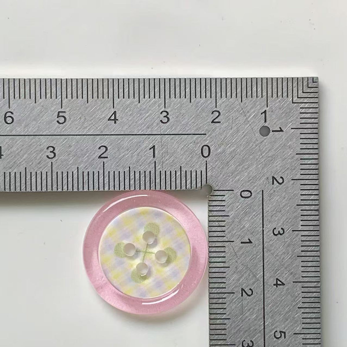 Pink rim floral four hole button beside ruler