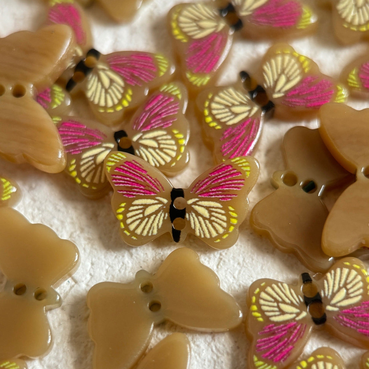 Tan butterfly-shaped two-hole buttons with pink wing accents
