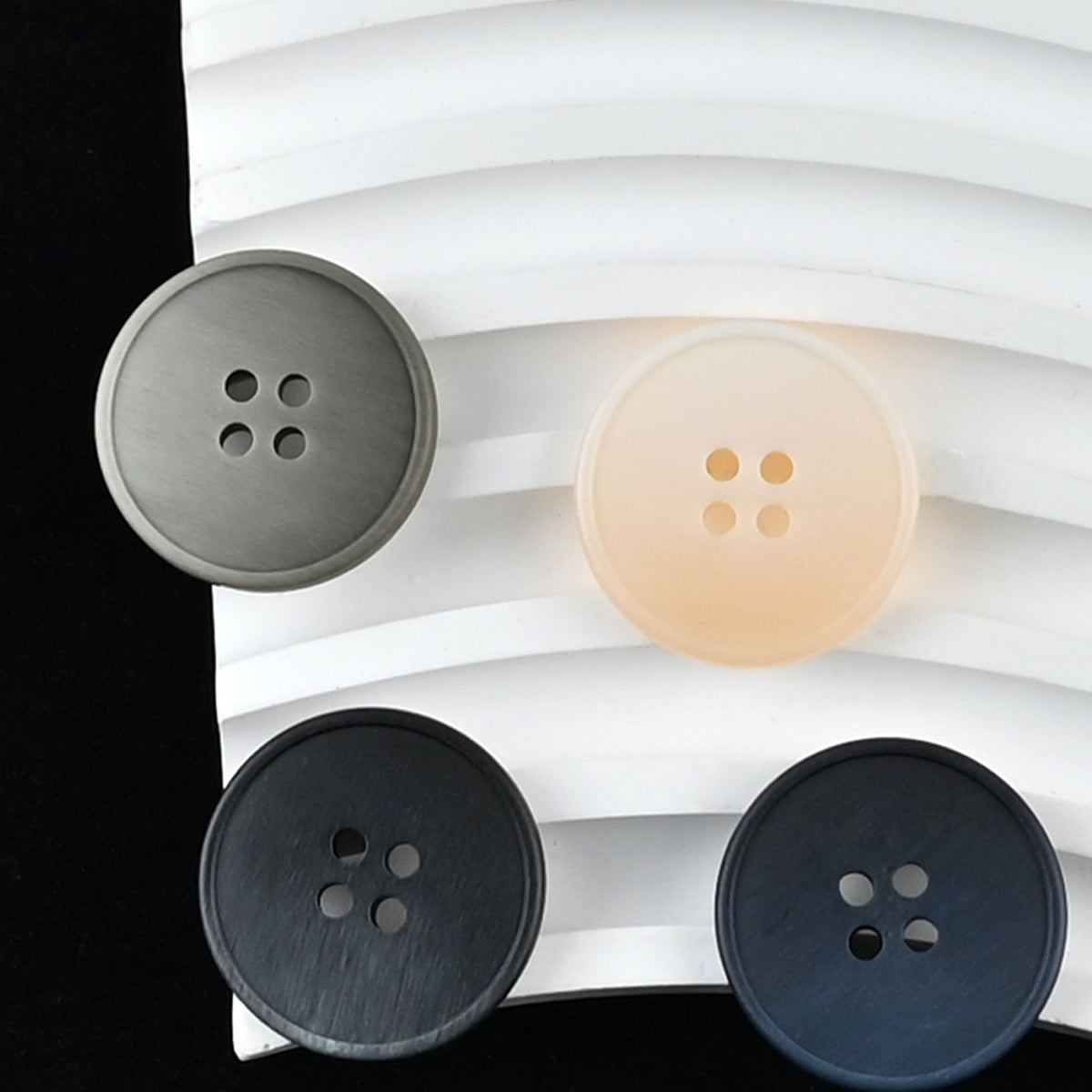 Beige, gray, black-gray, and navy four-hole buttons on curved white layers