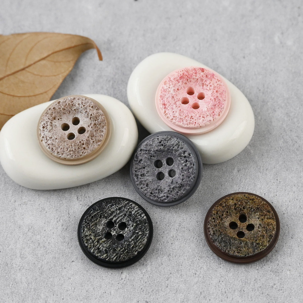 Five color four-hole buttons with pitted faces on a gray backdrop