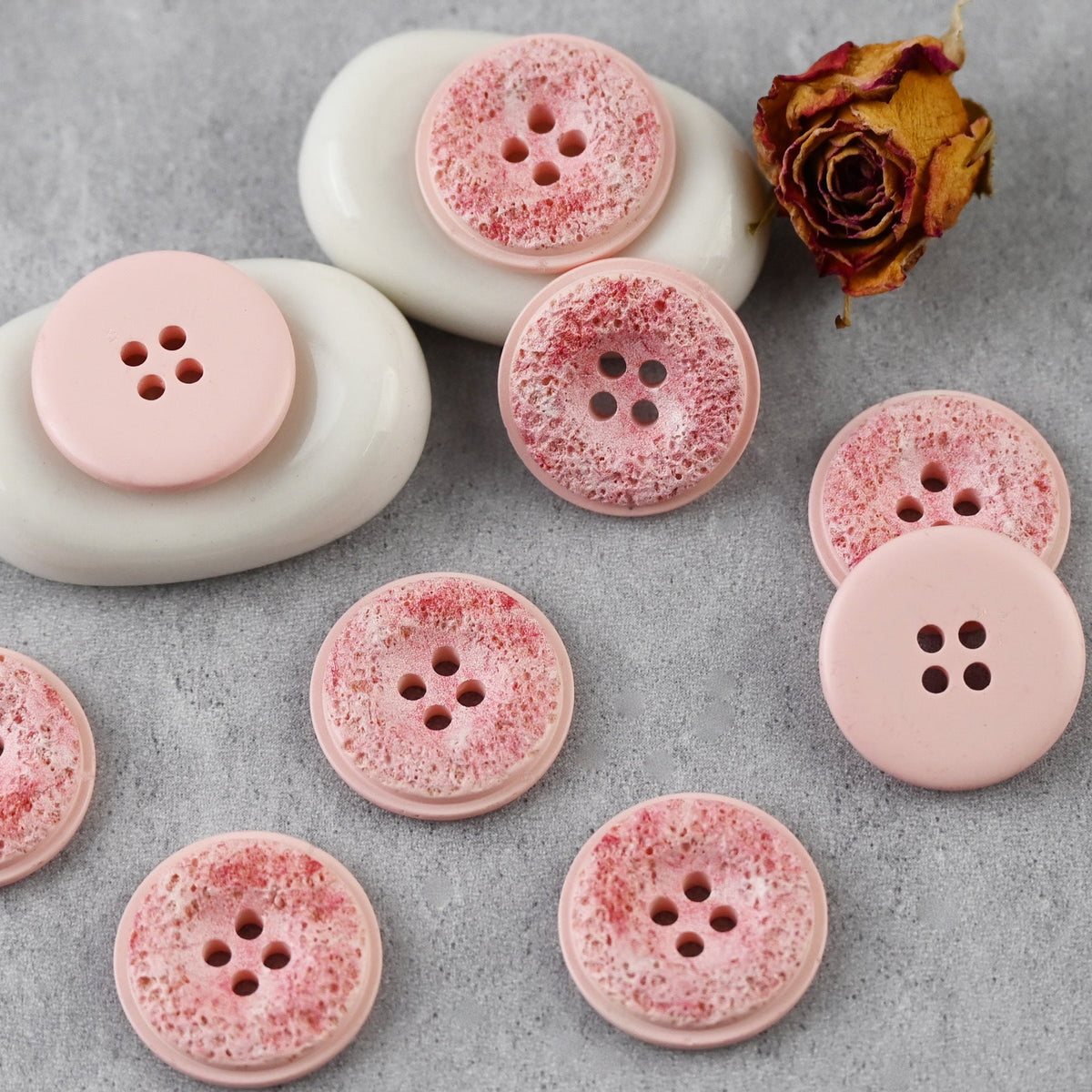 Pink pitted four-hole buttons beside a dried rose