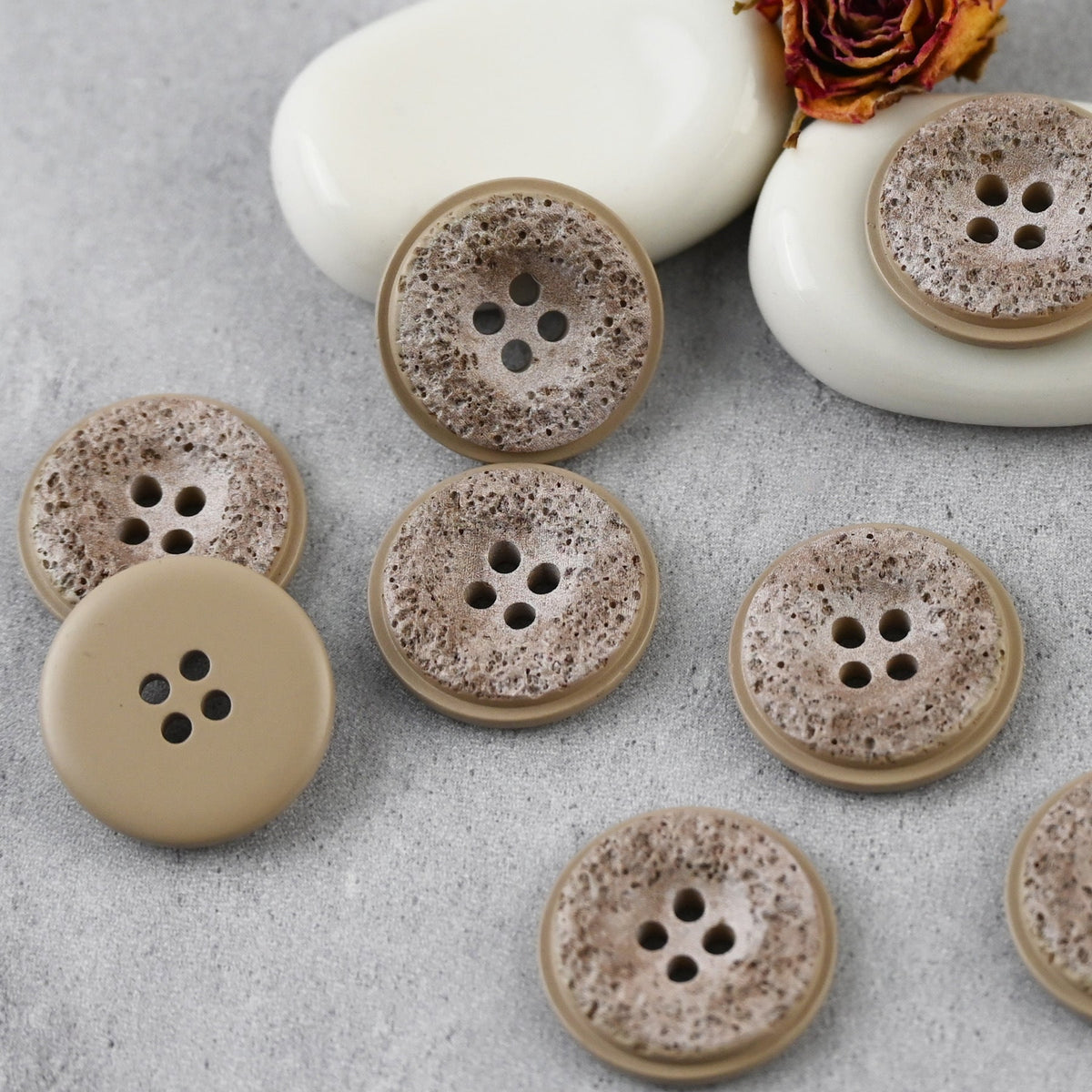 Khaki pitted four-hole buttons arranged on a gray backdrop