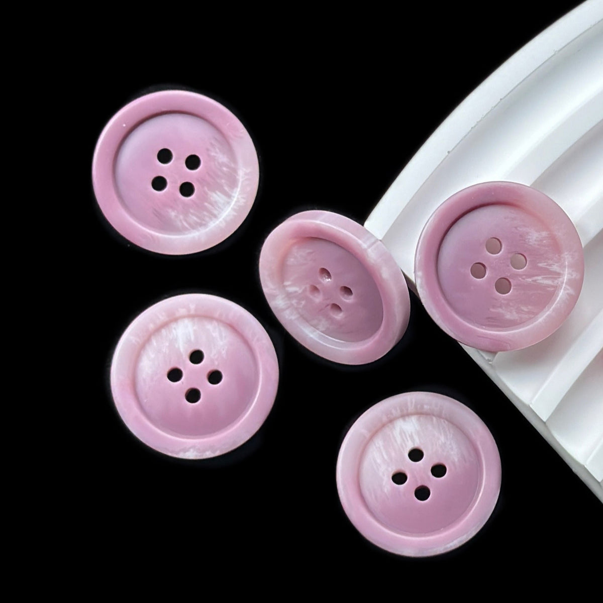 Lavender four-hole buttons with raised rims on a black background